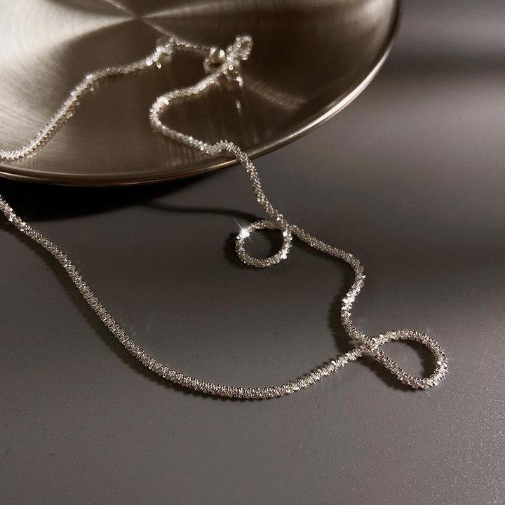 Silberne Halskette auf Metallplatte, elegantes Schmuckdesign, glänzend, minimalistisch.
