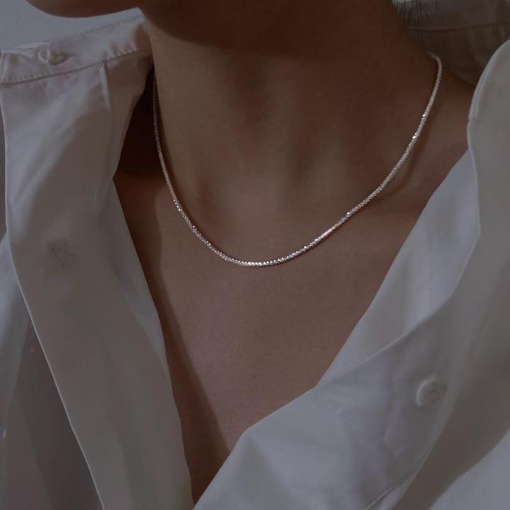 Silberne Halskette auf weißem Hemd, eleganter Schmuck für Damen, minimalistisches Design.