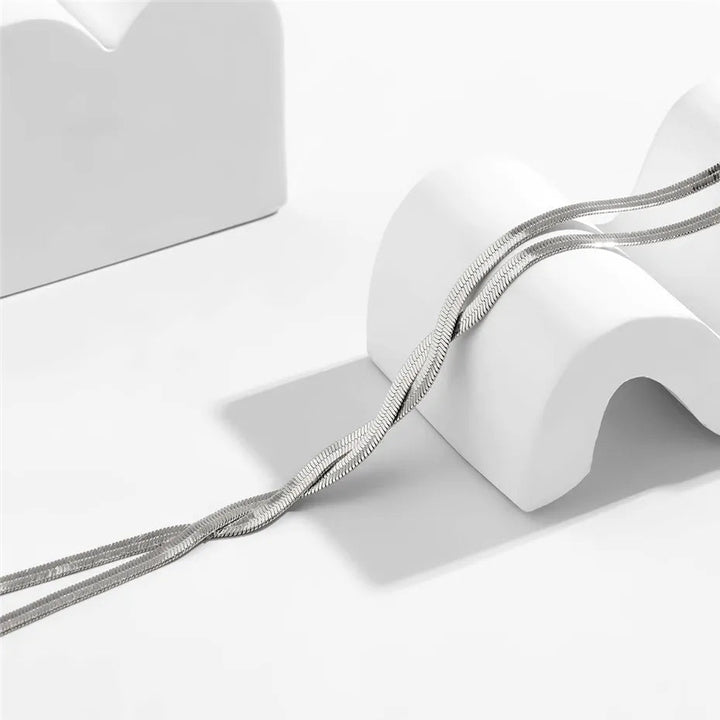 Silberne Schlangenkette auf weißem Hintergrund, elegantes Schmuckdesign, minimalistisch.