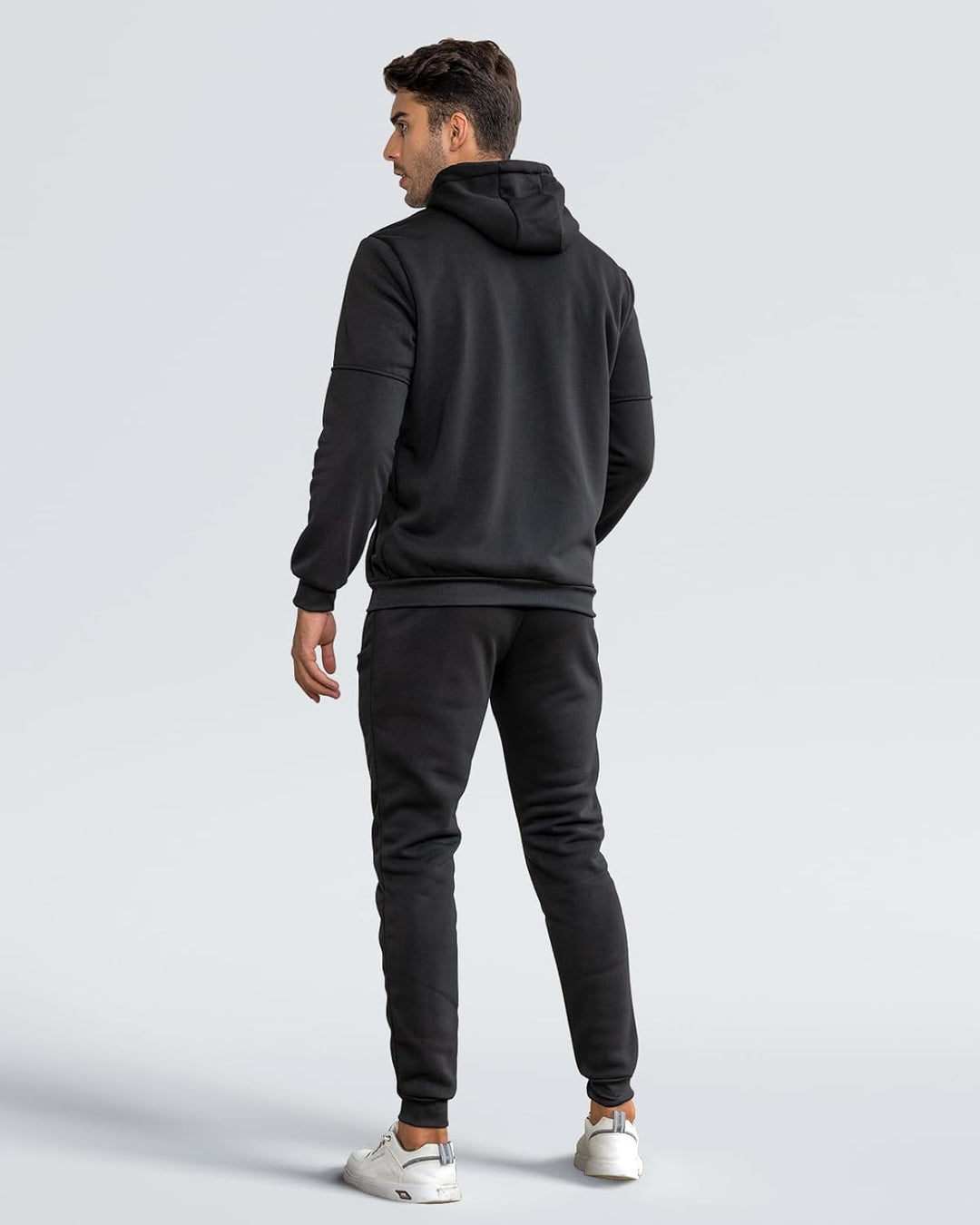 Mann in schwarzem Hoodie und Jogginghose, Rückansicht, sportliche Freizeitkleidung, grauer Hintergrund.