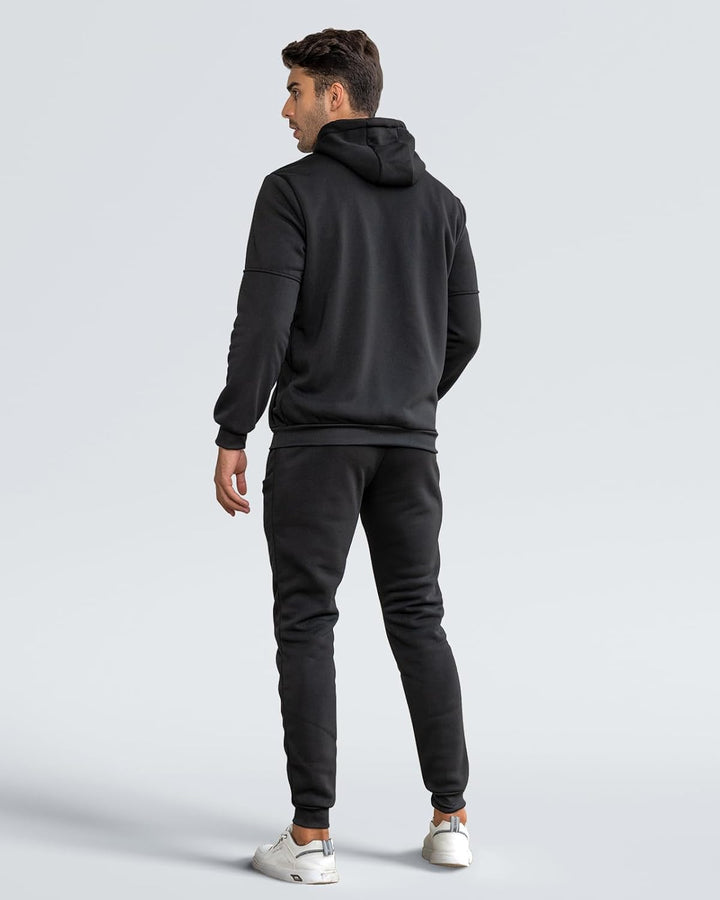 Mann in schwarzem Hoodie und Jogginghose, Rückansicht, sportliche Freizeitkleidung, grauer Hintergrund.