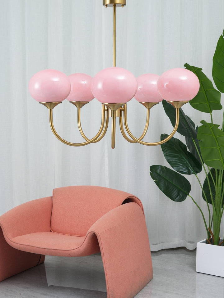 Rosa Kronleuchter mit goldenen Armen, modernes Design, über rosa Sessel, vor weißen Vorhängen.