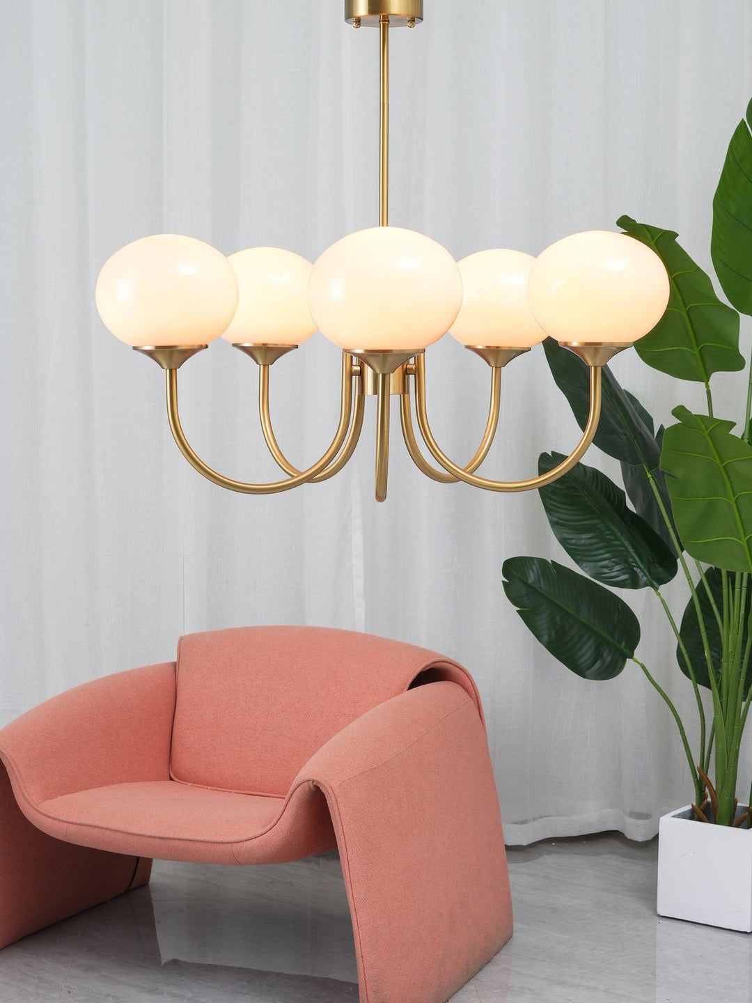 Goldene Kronleuchter mit runden Lampen, rosa Sessel, moderne Inneneinrichtung, Pflanzen.