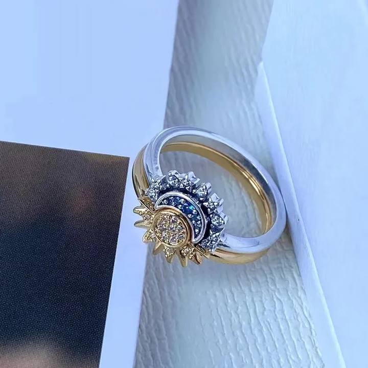 Goldener und silberner Ring mit Sonnenmotiv, blauen und klaren Kristallen, elegantes Schmuckdesign.