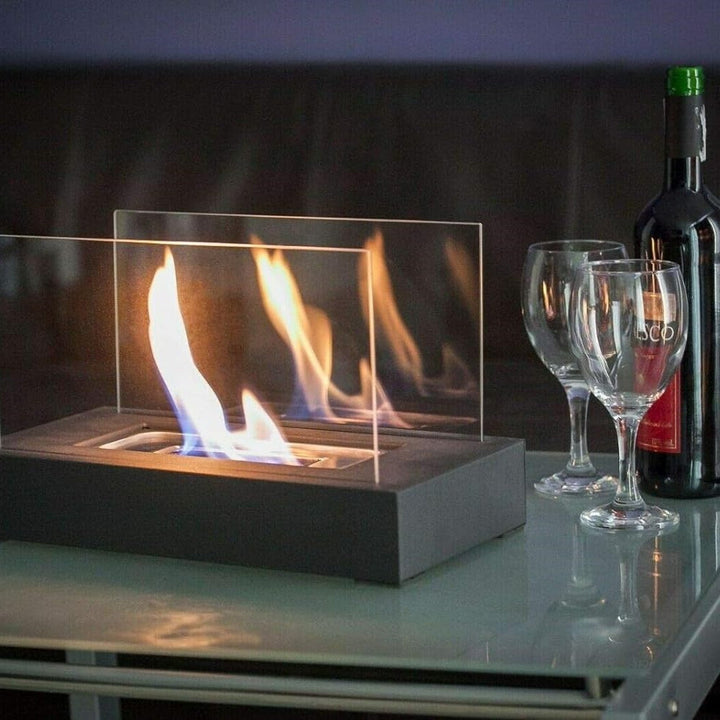 Tischkamin mit Glaswänden, Flamme, Weinflasche und Gläser auf Glastisch, modernes Design.
