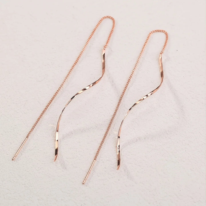 Roségoldene, lange Ohrringe mit geschwungenem Design, filigrane Kette, eleganter Schmuck.