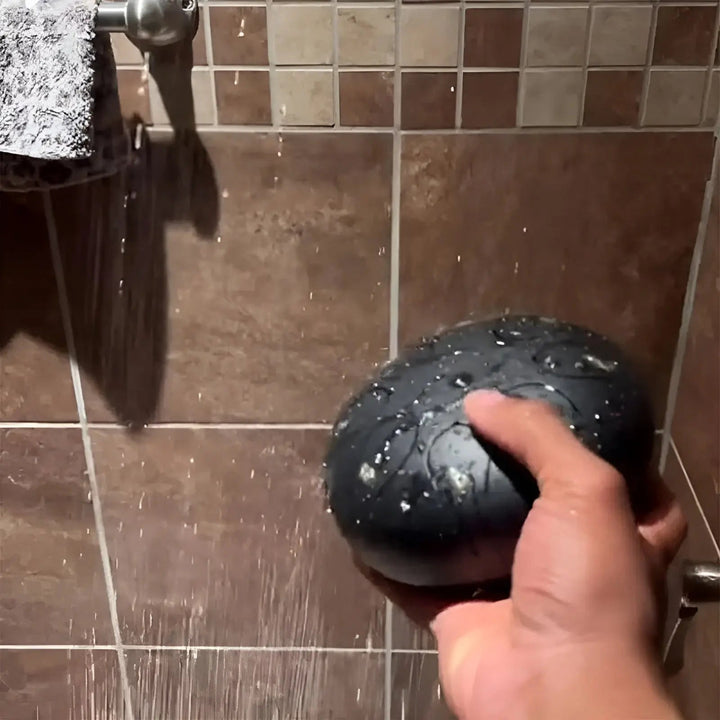 Hand hält schwarze Stahlzungentrommel unter Wasser im Badezimmer.