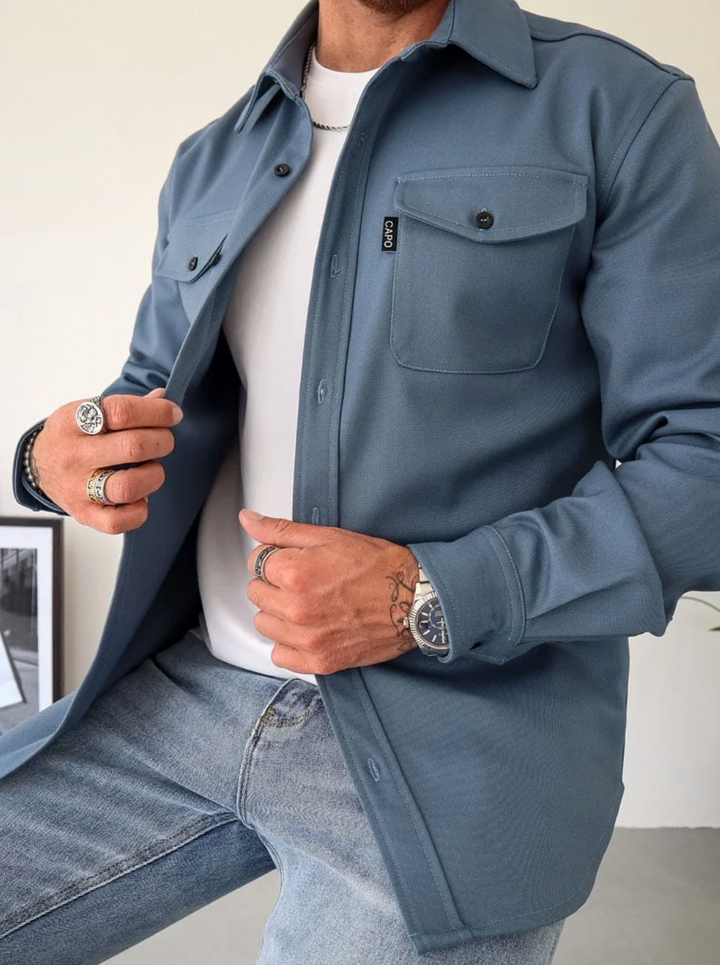 Mann in blauem Hemd, Jeans, weiße T-Shirt, trägt Ringe und Uhr, Herbstmode.