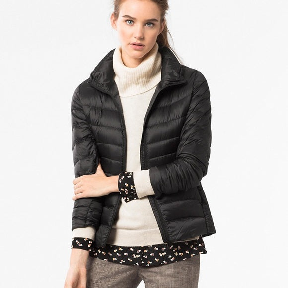 Frau trägt schwarze Daunenjacke, cremefarbenen Rollkragenpullover, modisch, elegant.