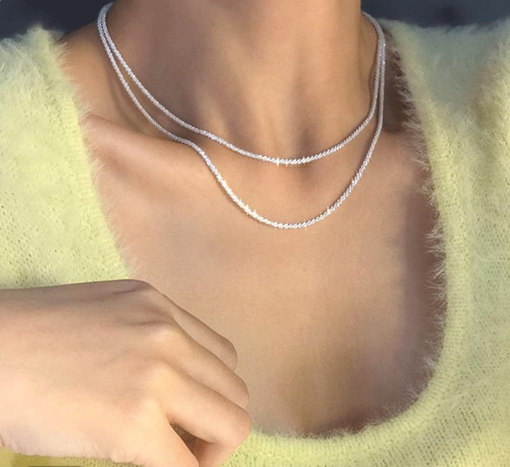 Doppelte Silberkette auf gelbem Pullover, eleganter Schmuck, Damenmode, Accessoire.