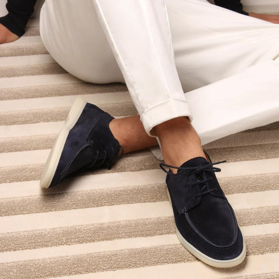 Dunkelblaue Wildleder-Sneaker für Herren, lässig, mit weißer Sohle, auf gestreiftem Teppich.