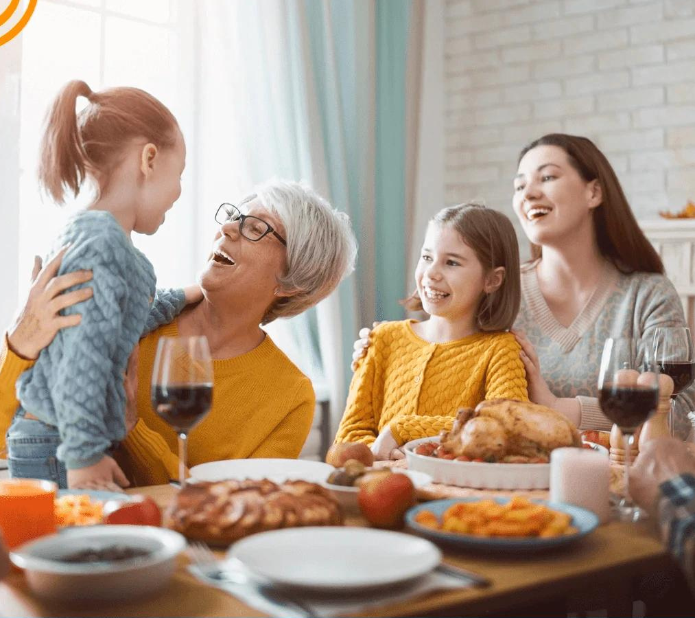 Familie beim Essen, lächelnd, mit gedecktem Tisch, Huhn, Wein, gemütliche Atmosphäre, Tageslicht.