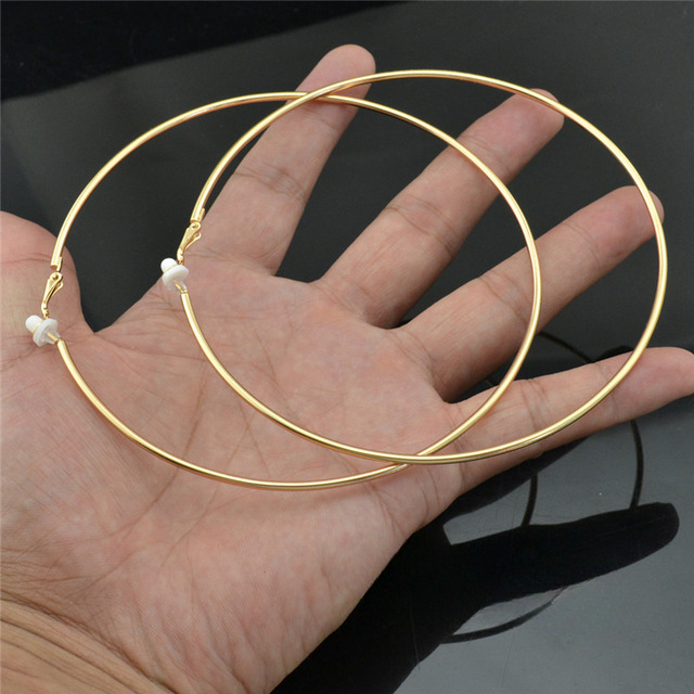 Goldene Creolen Ohrringe, großer Durchmesser, auf Handfläche, Schmuckaccessoire, glänzend.