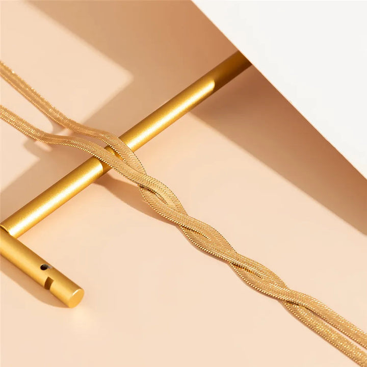 Goldene Halskette aus Edelstahl, gedrehtes Design, auf beigem Hintergrund, Schmuckfotografie.