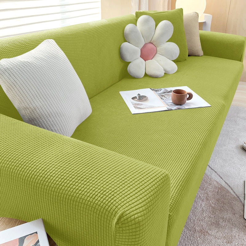 Grünes Sofa mit Blumen-Kissen, Kaffeetasse und Zeitschrift auf hellem Teppich im Wohnzimmer.