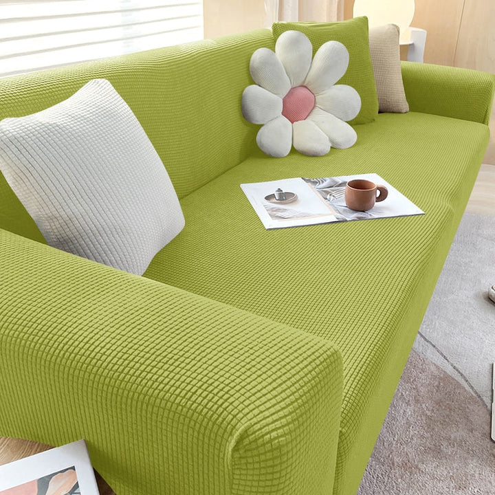 Grünes Sofa mit Blumen-Kissen, Kaffeetasse und Zeitschrift auf hellem Teppich im Wohnzimmer.