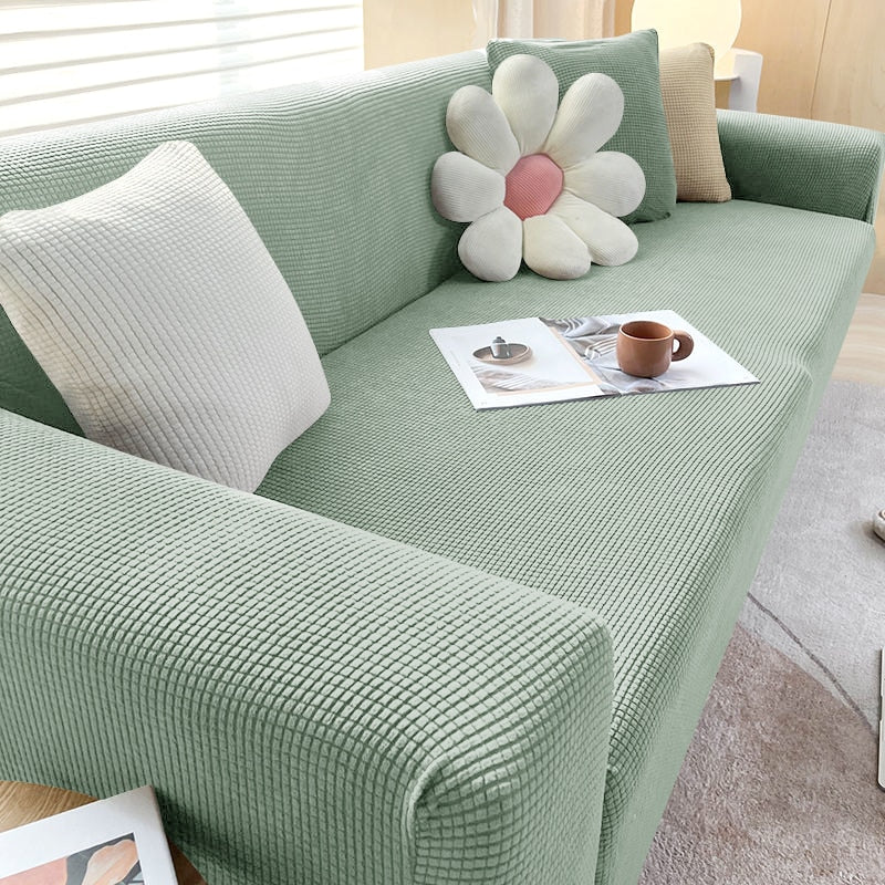 Grünes Sofa mit Blumen-Kissen, Kaffeetasse und Zeitschrift, modernes Wohnzimmer, Tageslicht.