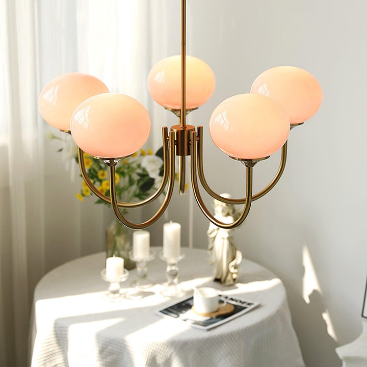 Moderne Kronleuchter mit rosa Glaskugeln, goldene Metallarme, über Tisch mit Kerzen.
