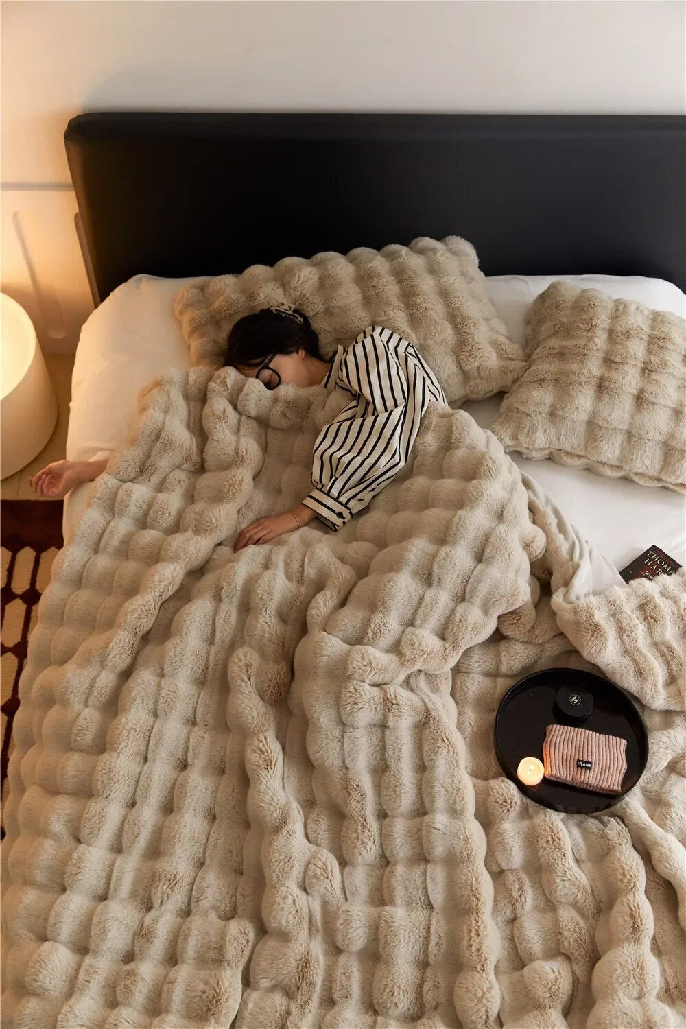 Frau schläft auf Bett mit beiger, plüschiger Decke und Kissen, gemütliches Schlafzimmerambiente.